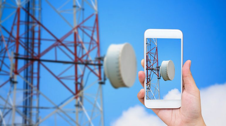 hand hold mobile smartphone with telecommunication tower and satellite antennas wireless technology on blue sky background